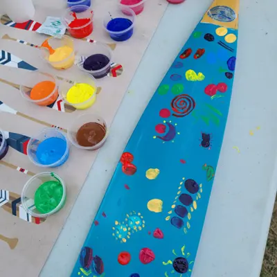 A rowing paddle with blue paint and various coloured painted designs 