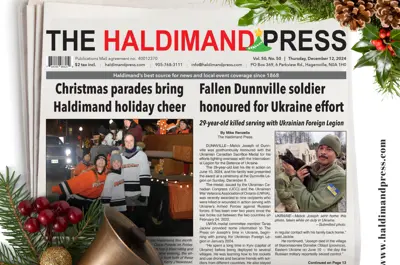 A local newspaper sits on a table surrounded by greenery and holiday decorations
