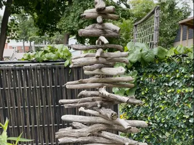 A crafted tree made from driftwood pieces sits outside in a yard