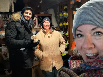 A woman holds a pair of alpaca socks and smiles while two people stand behind with displays of alpaca wool products