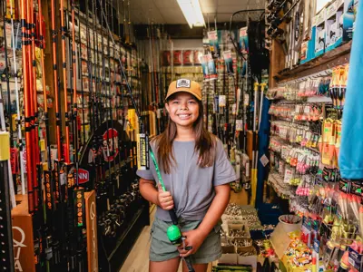A girl holds a bright green fishing rod in a store