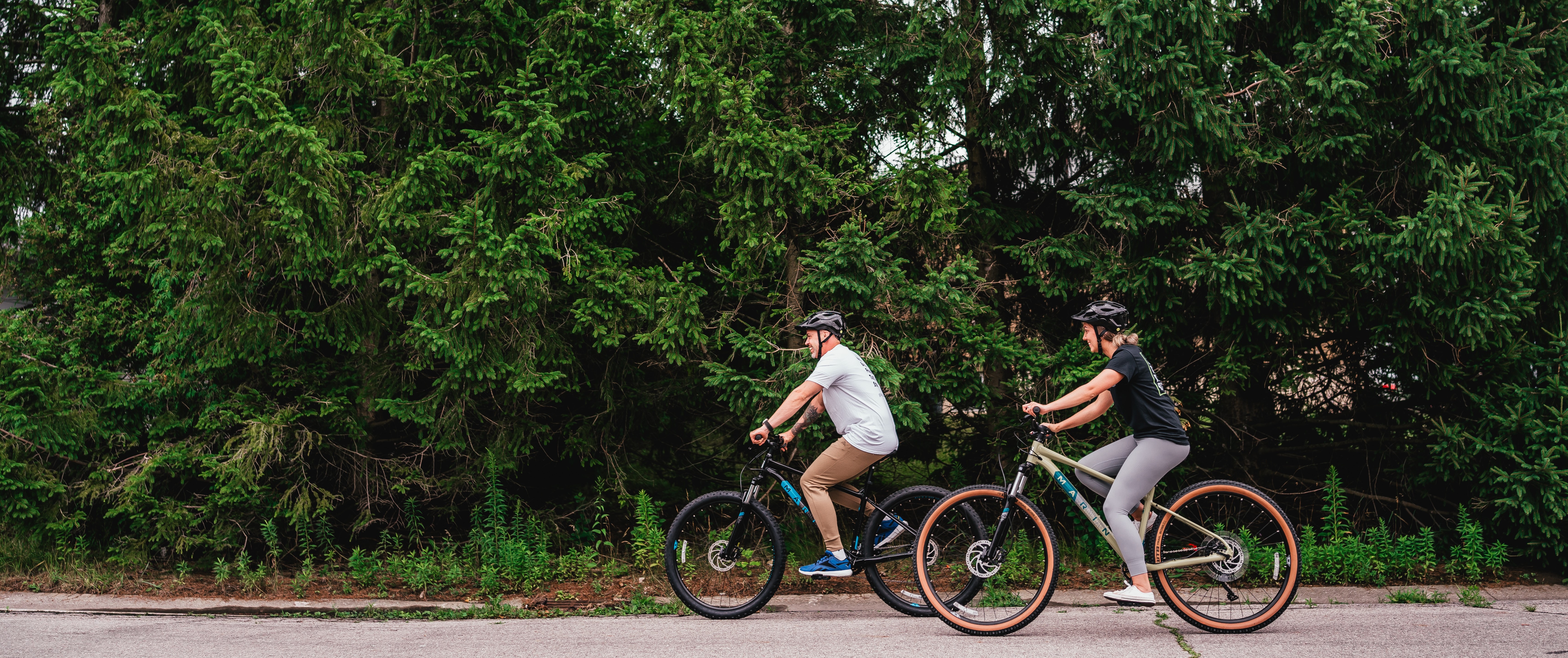 man and woman cycling by a line of trees