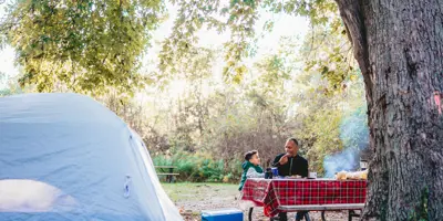 man and boy eating at a picnic table beside a camping tent 