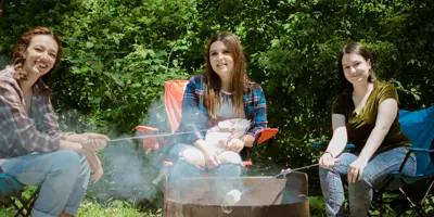 Young women sit around a campfire roasting marshmallows