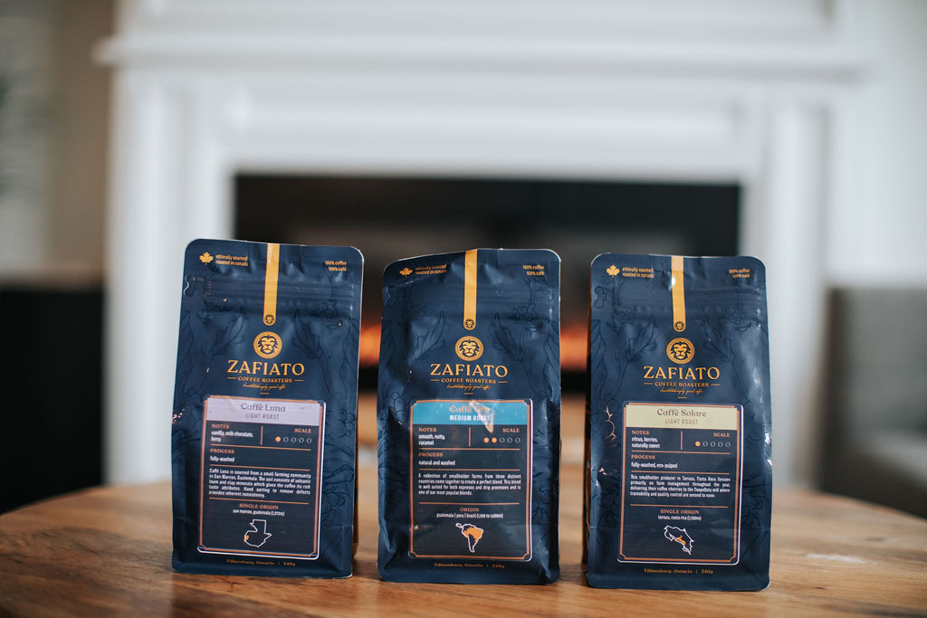 Three bags of coffee sit on a wooden table in front of a fireplace