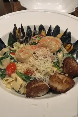 A plate of mixed seafood over creamy linguini sits on a white plate