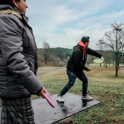 man and woman throwing discs playing disc golf