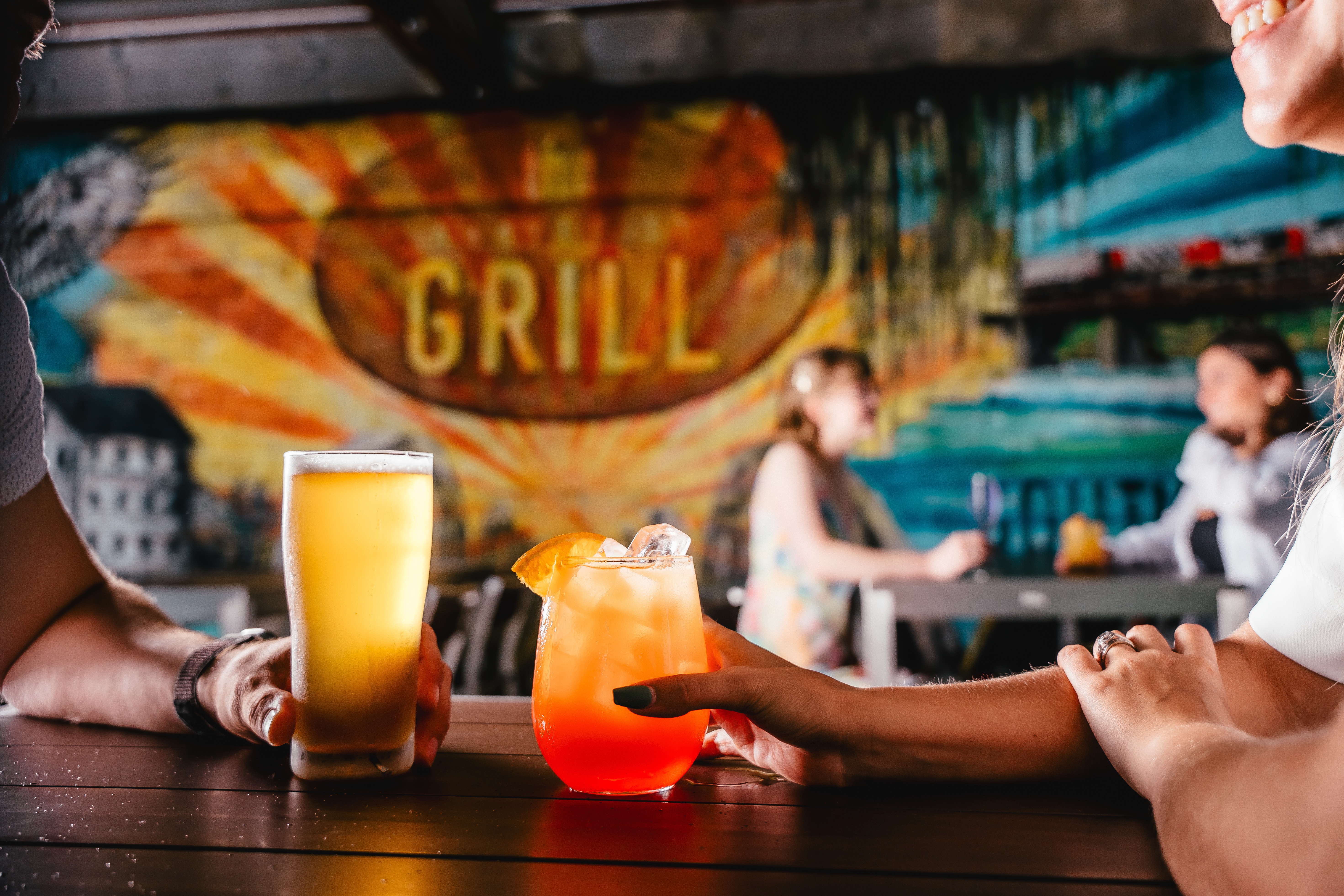 Two colourful cocktails are backlit and are sitting on a bar