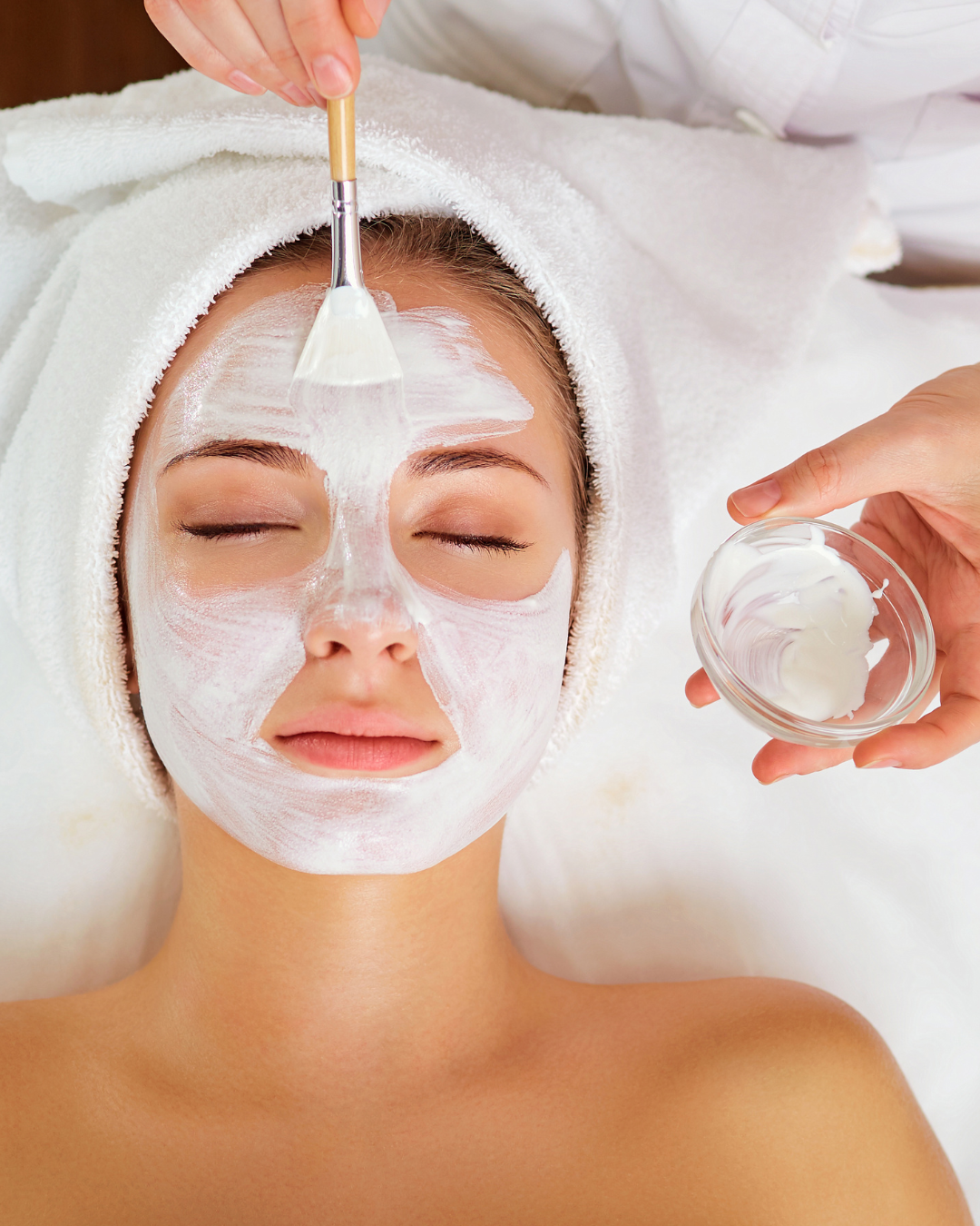 A woman getting a facial has white cream painted on her face