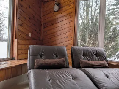 Two comfy chaises sit in a window overlooking a snowy backdrop