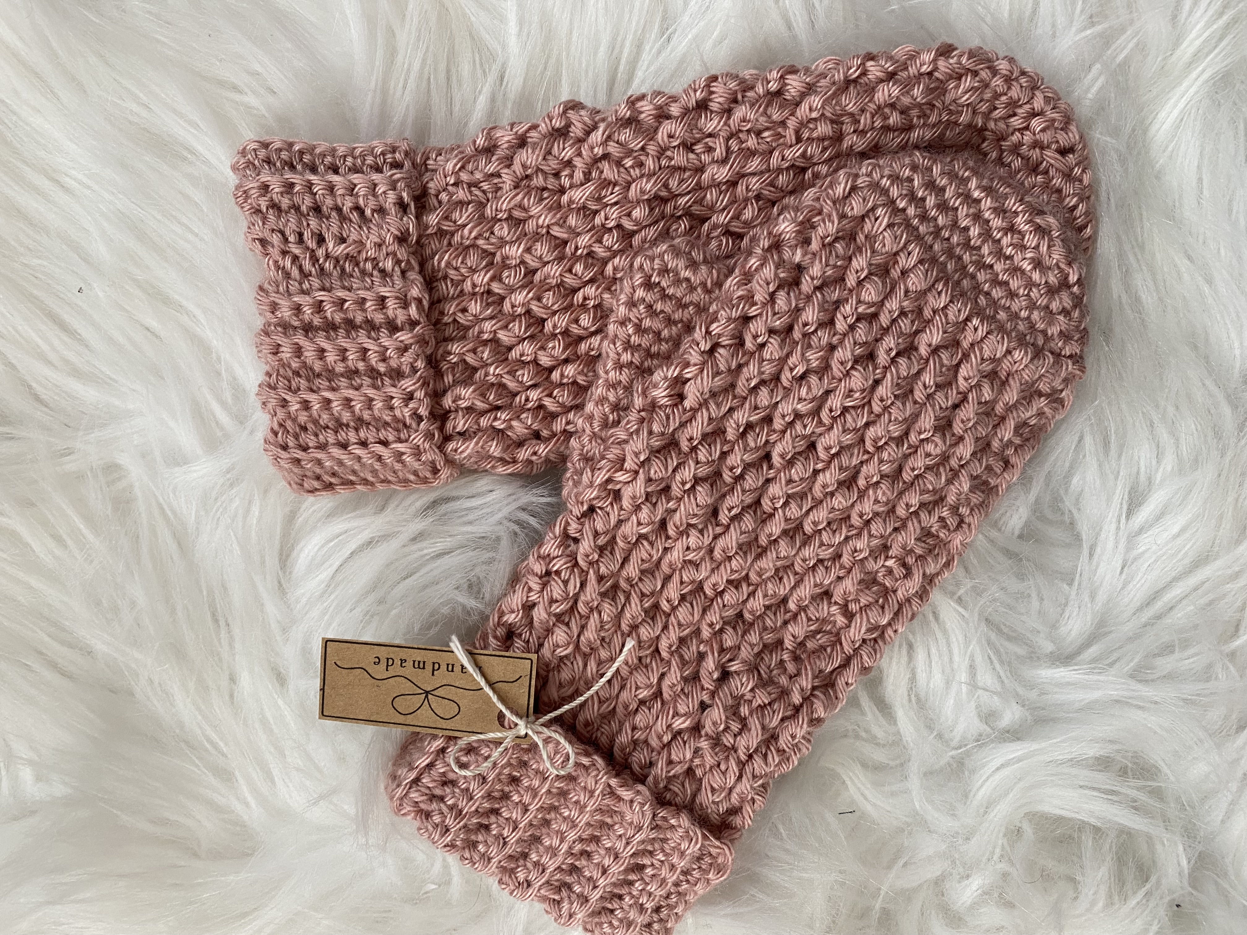 A pair of rose coloured hand-knit mittens sit on a white fur