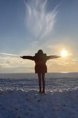 A woman stands with arms outstretched in front of a frozen lake