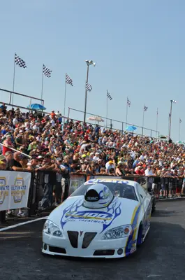 A race car sits in front of a large bandstand full of people