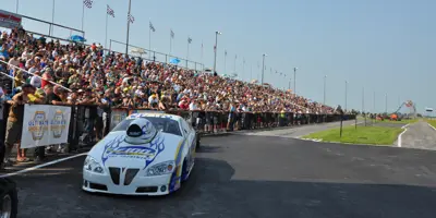 A race car sits in front of a large bandstand full of people