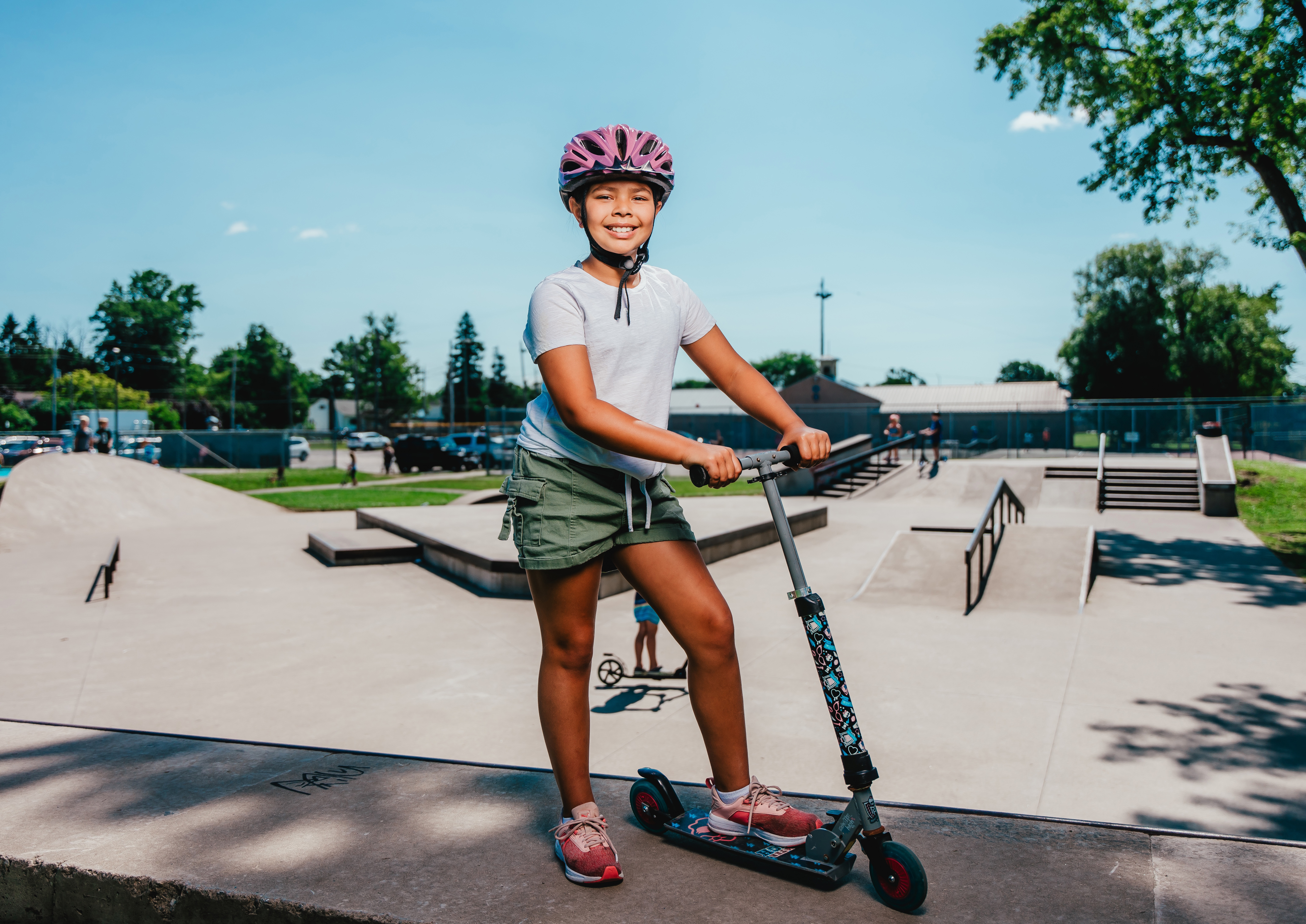 A girl in a helmet stands on a razor scooter in a skate park