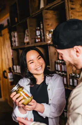 A woman and man smile over a jar of pickles