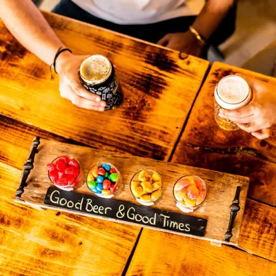 a board with a variety of candies, and two people holding beers behind