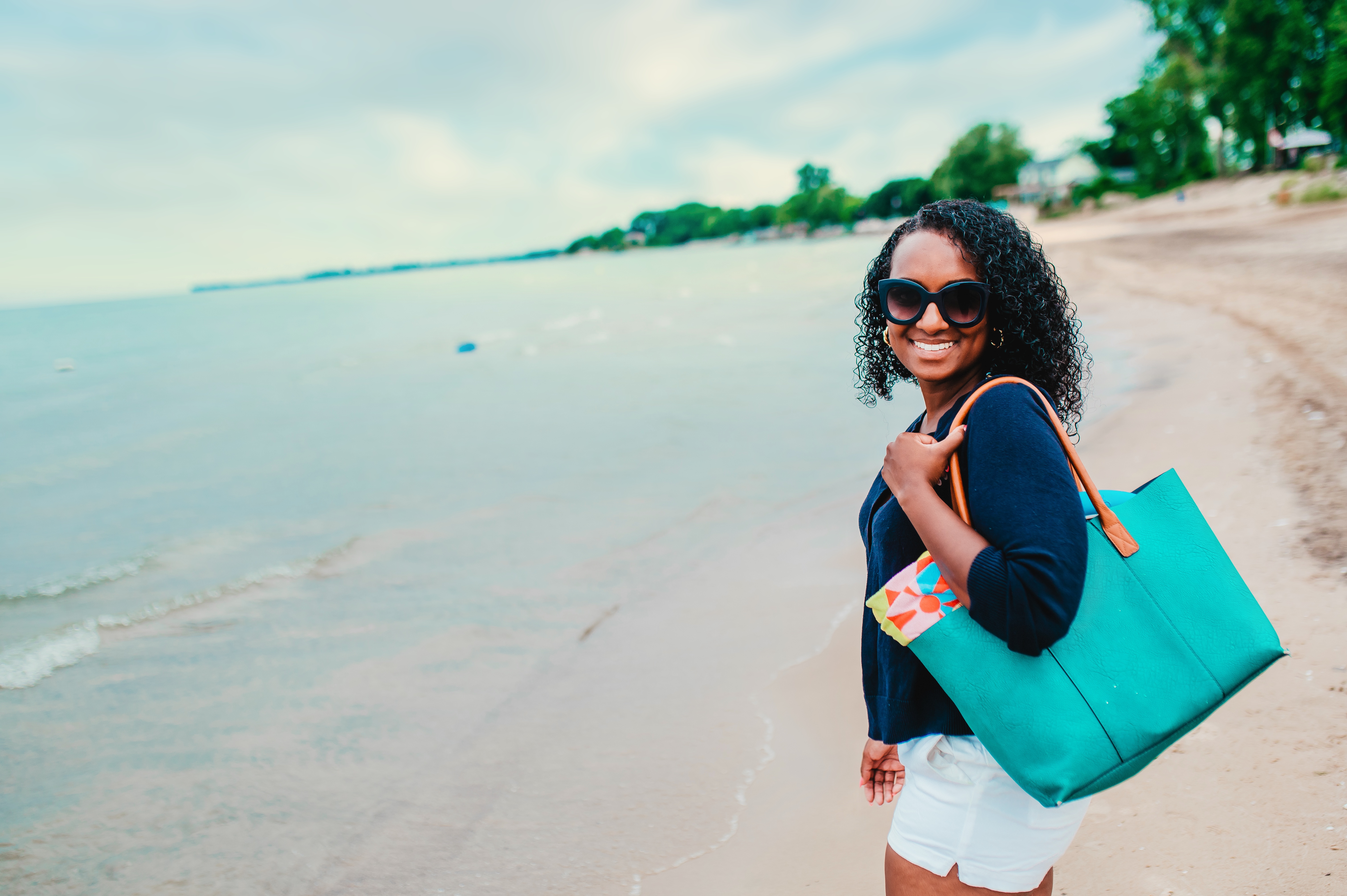 A woman holding a bright beach bag walks along the waters edge