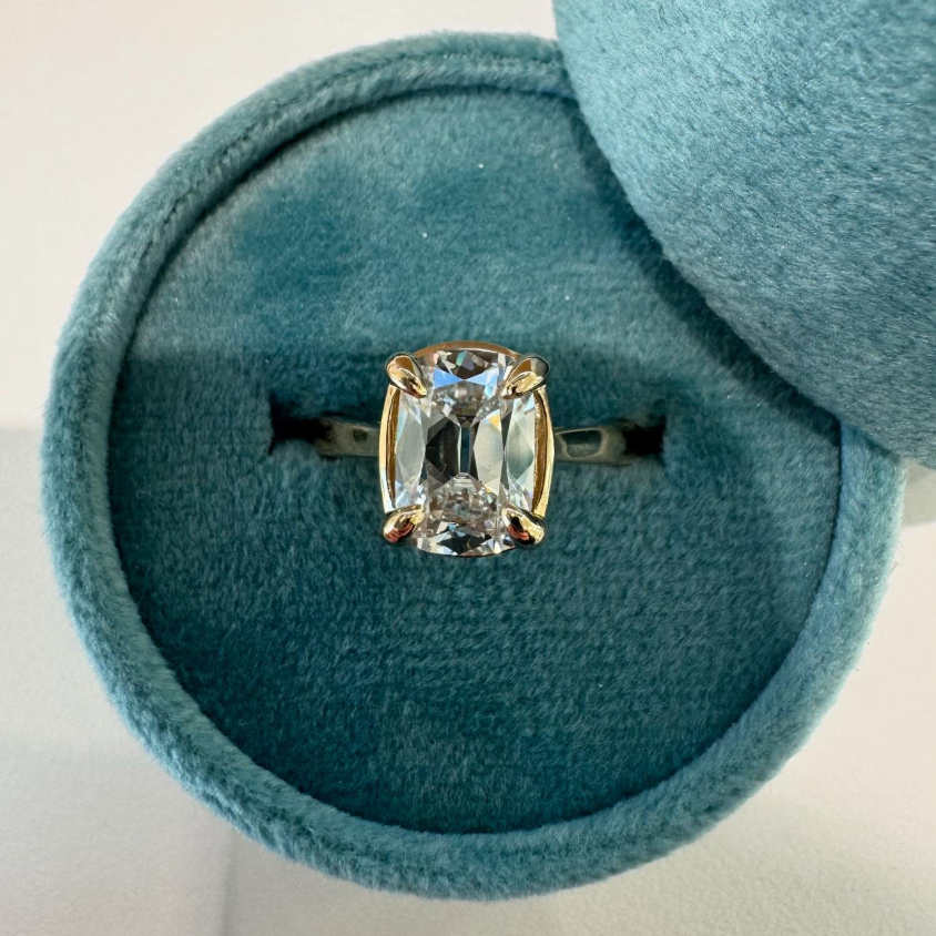 An cushion cut engagement ring sits in a blue velvet box