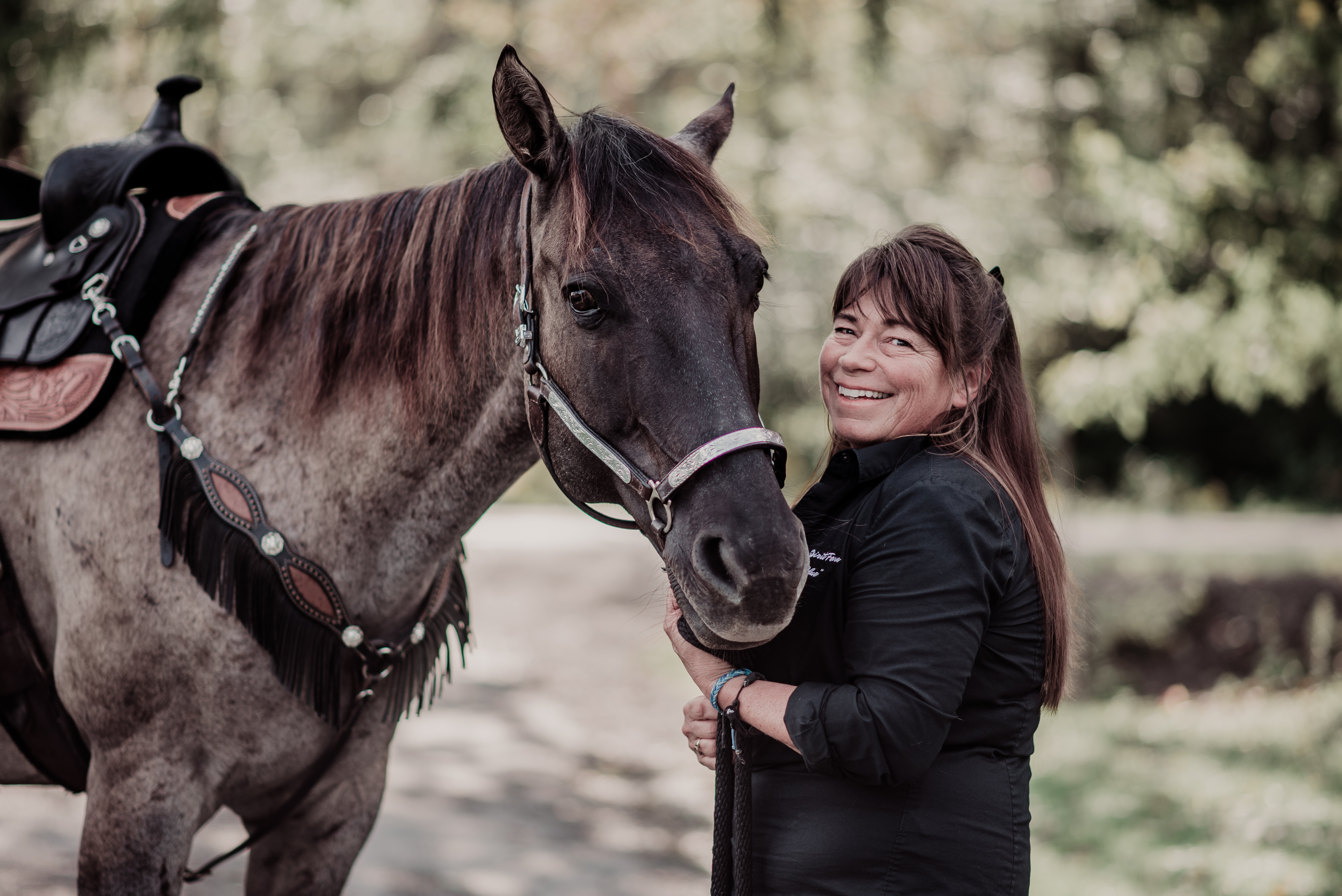 A woman stands next to a horse's head and holds its reins