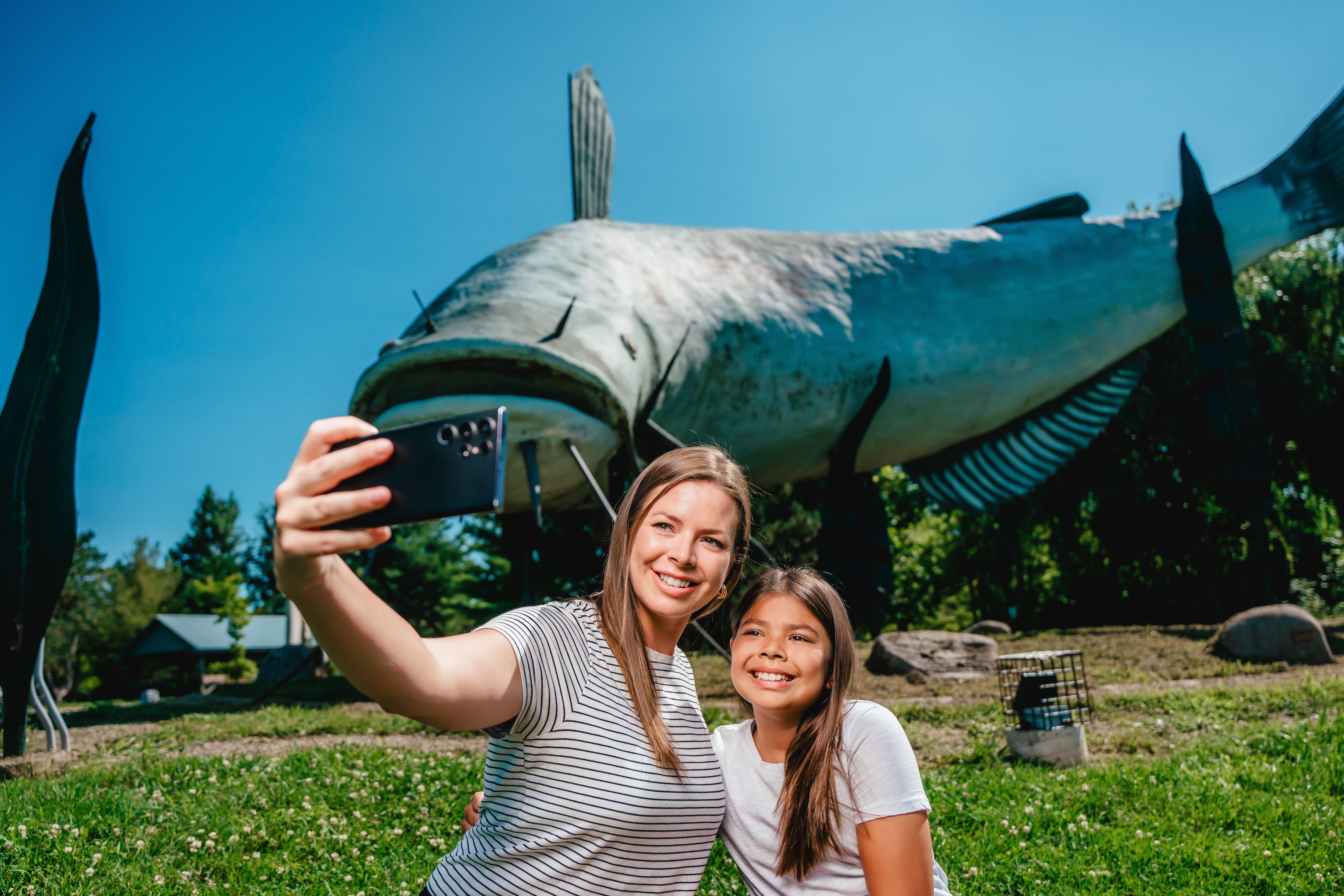 A mother and daughter take a selfie in front of a giant mudcat