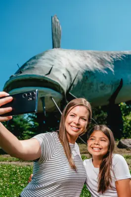 A mother and daughter take a selfie in front of a giant mudcat