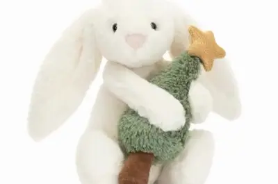 A stuffed white bunny holds a stuffed Christmas Tree with a gold star on top