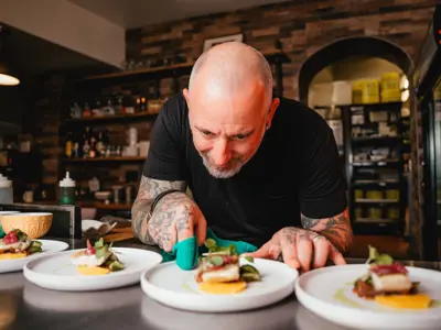 A chef plates up a row of dishes featuring fish filets with green herby sauce in an upscale restaurant