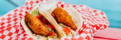 2 perch tacos in a basket on a red picnic table