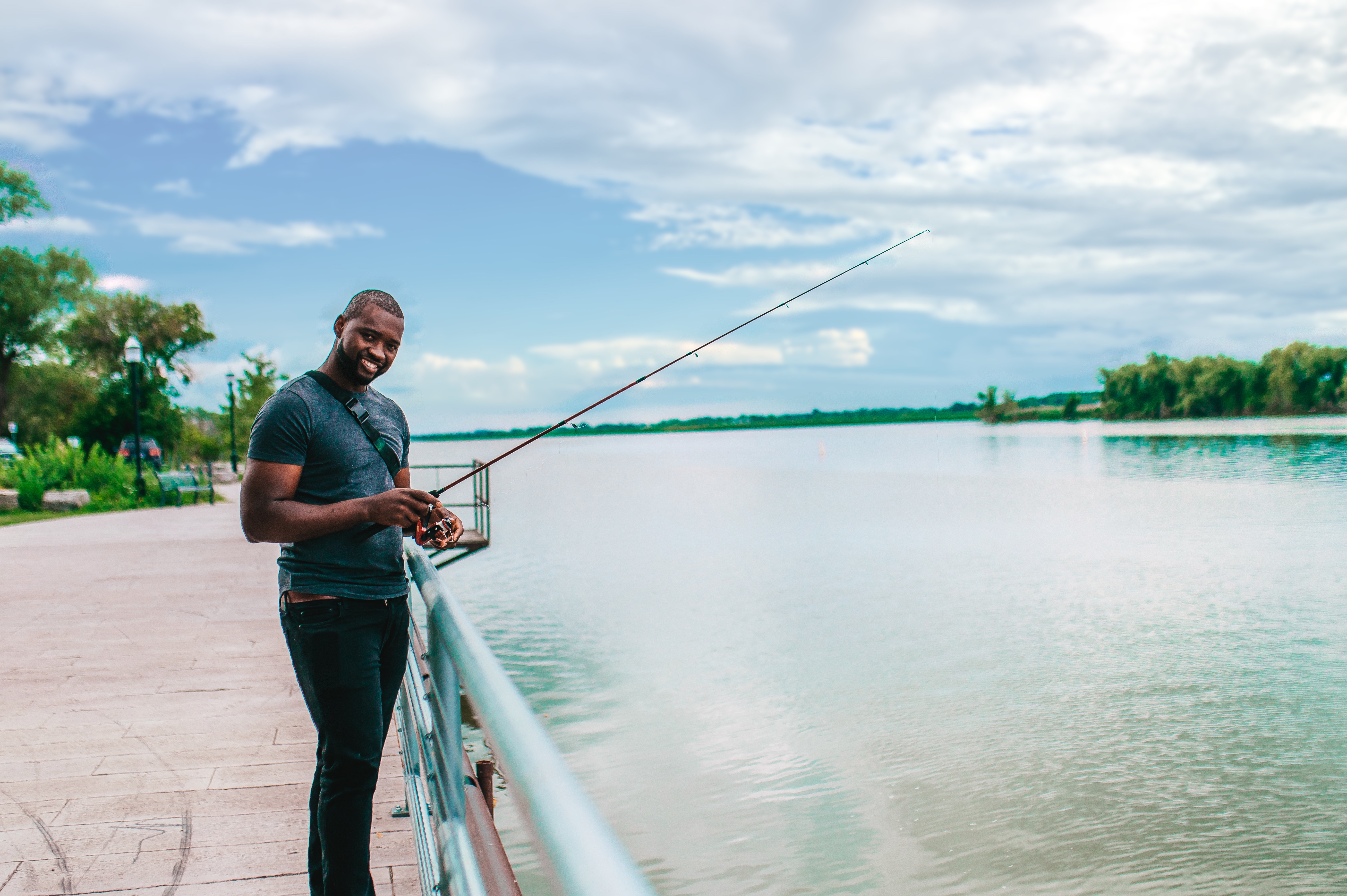 A man holds a fishing pole in a riverfront park