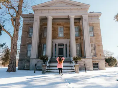 A woman walks towards a heritage mansion in a winter landscape
