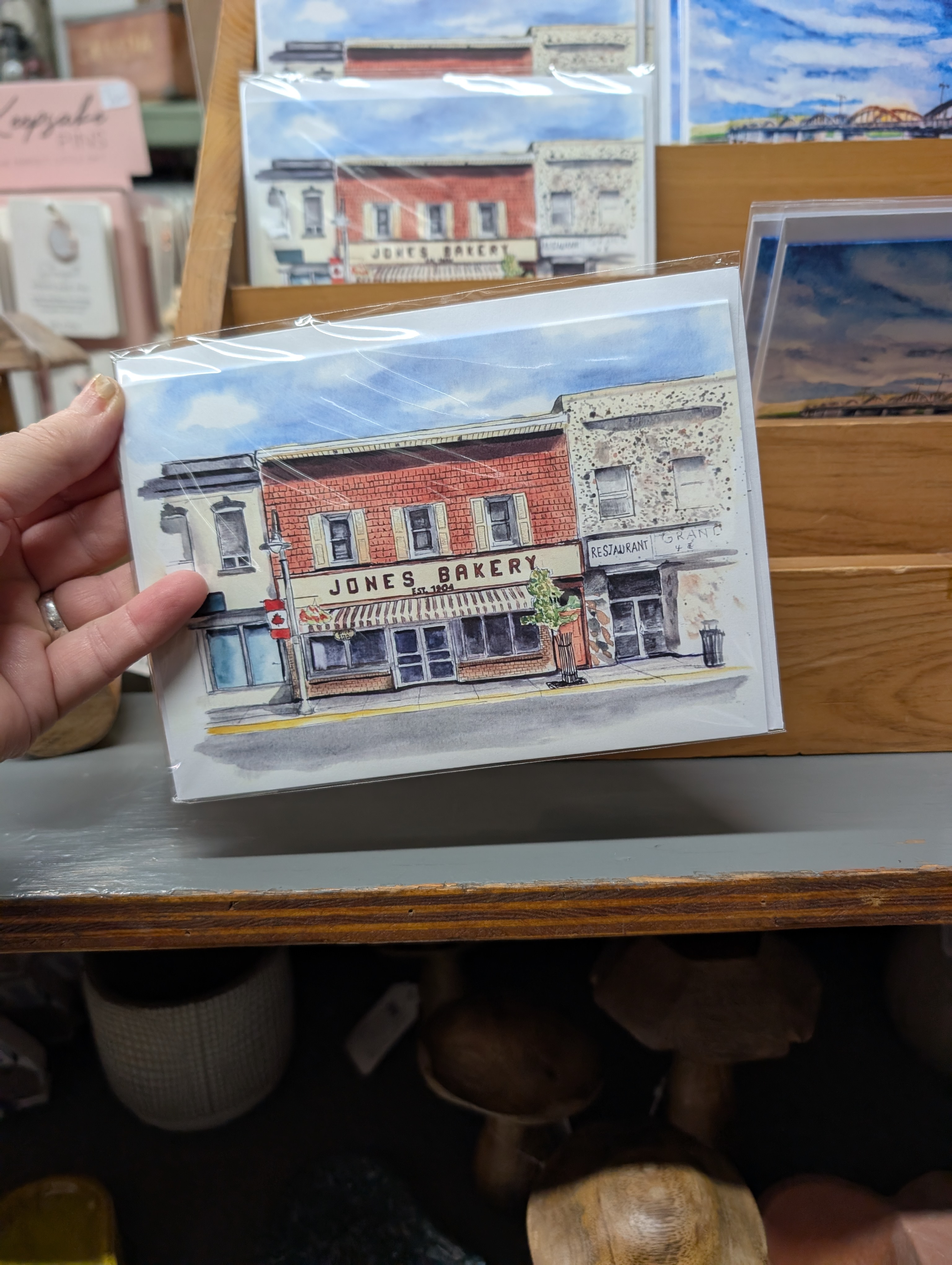 A woman's hand holds a hand drawn image of a bakery storefront