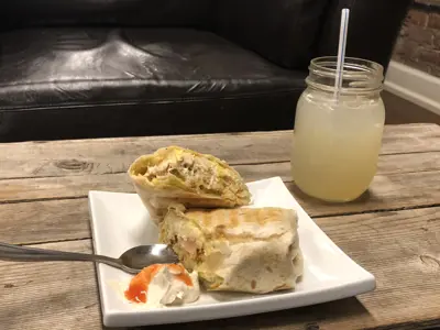 a wrap sits on a white plate with a lemonade in a mason jar next to it on a wooden table