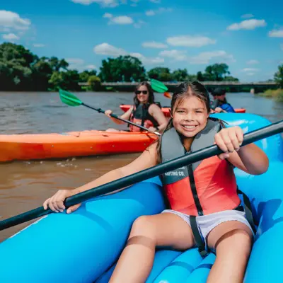 A river with a girl in a raft and other people in kayaks enjoying paddling