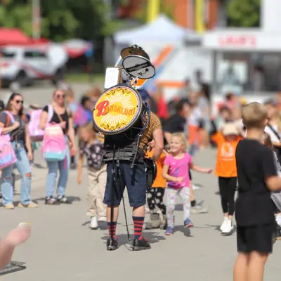 A one man band walks through a crowd at the fair
