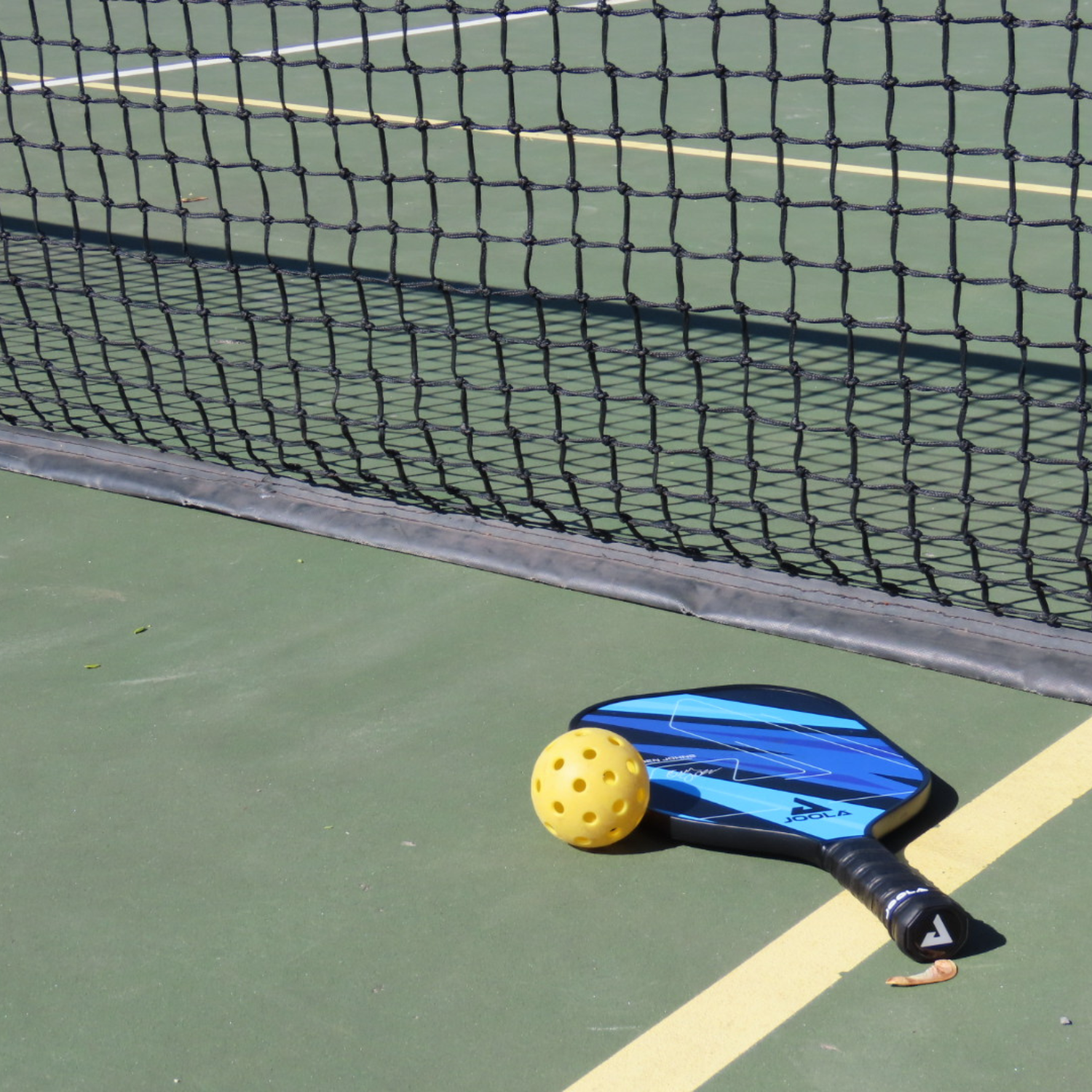 Pickleball paddle and ball on a court by the net